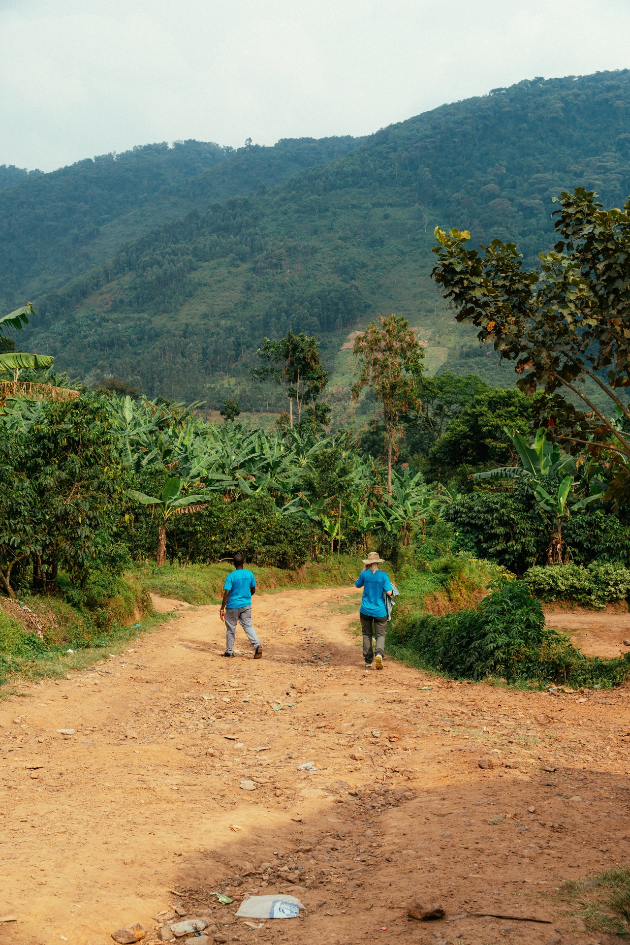 Two helpers on a dusty path through Uganda's green hills