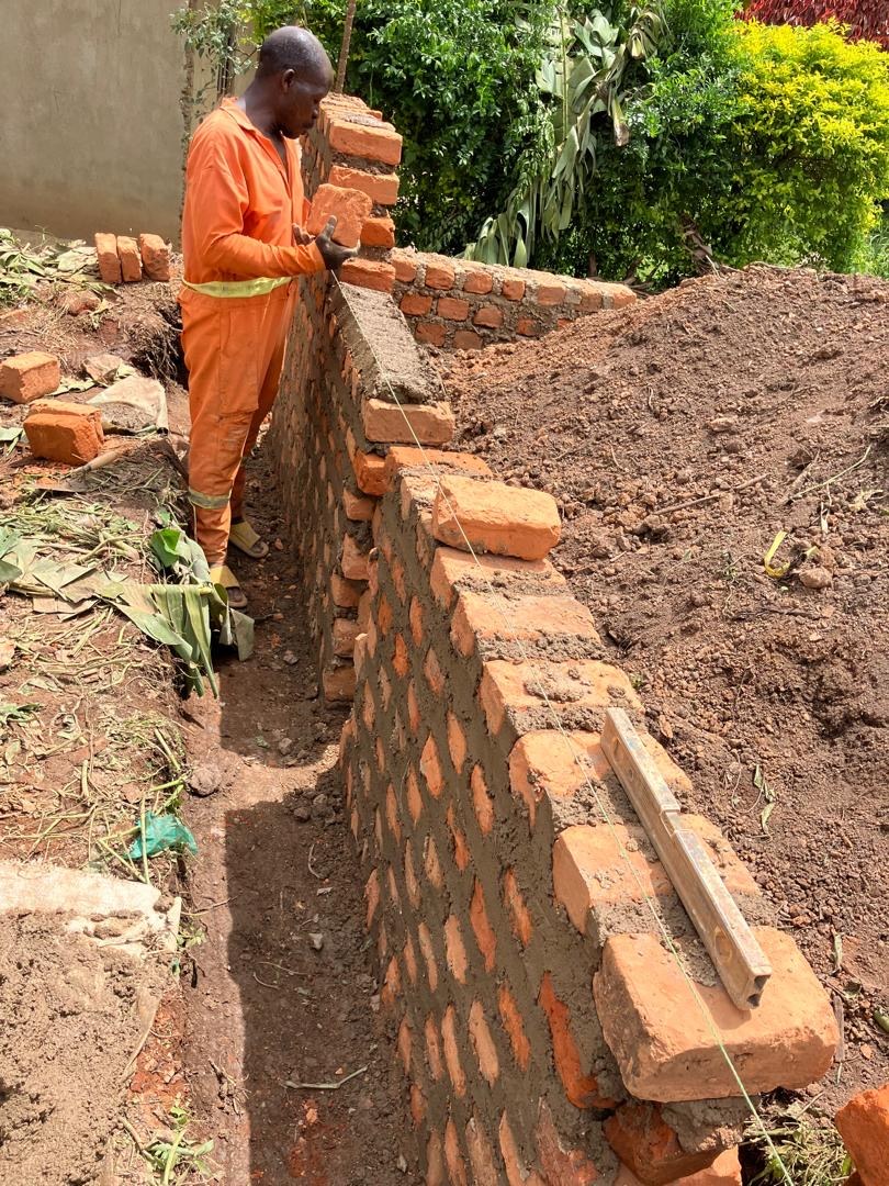 Foundation walls of HopeKitchen Buhoma being laid in April 2026 — clay bricks and cement mortar in a hand-excavated trench. Photo: Mark Suer