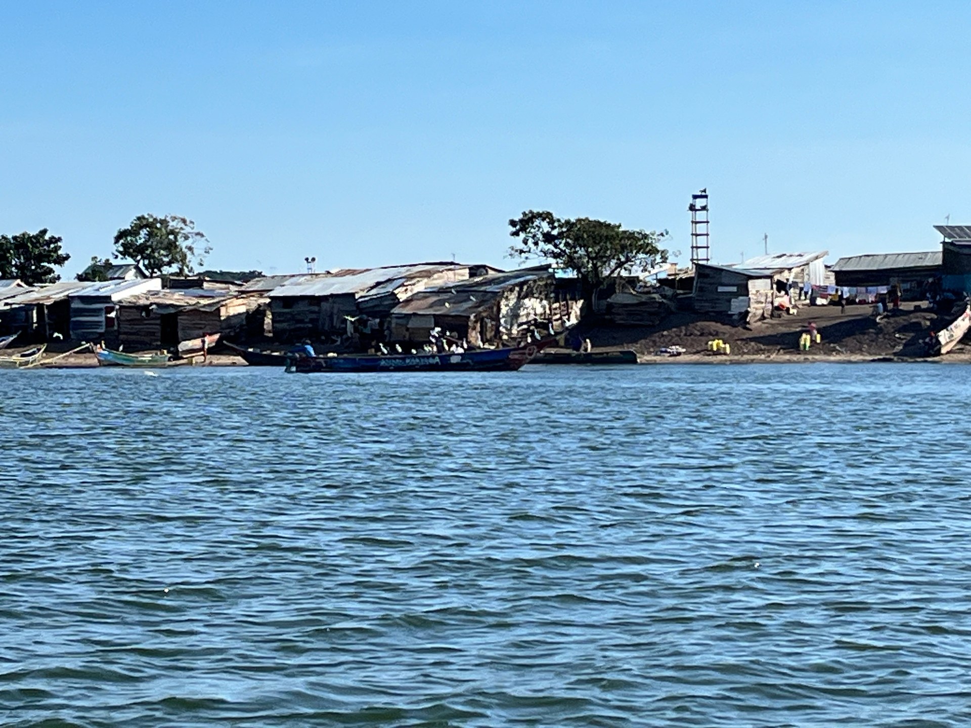 A fishing village on a small island in Lake Victoria seen from the boat to Ngamba Island — wooden huts, traditional boats, no electricity or running water. Photo: Mark Suer, October 2024, GPS: -0.0847, 32.6508
