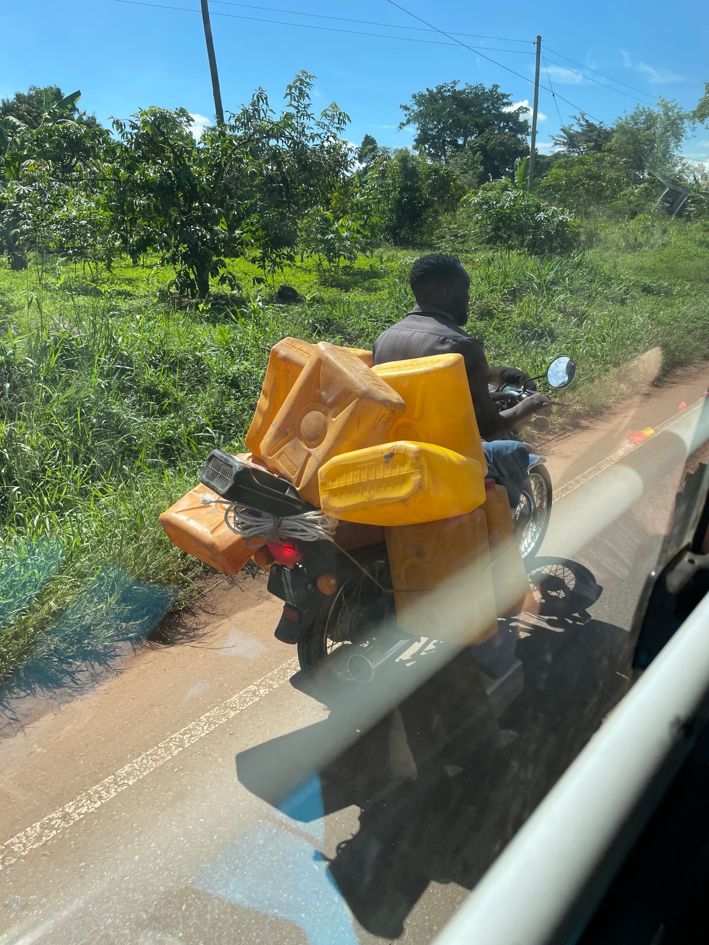 Boda-boda driver transporting water canisters on a motorcycle in rural Uganda. Photo: Mark Suer