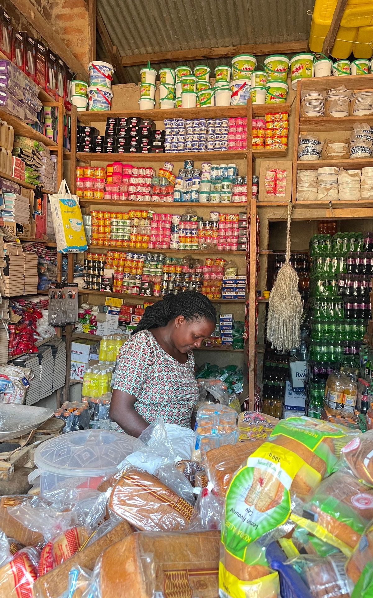 Local shop owner in Buhoma — beans, soap, bread and daily essentials on handmade wooden shelves, photographed January 2026