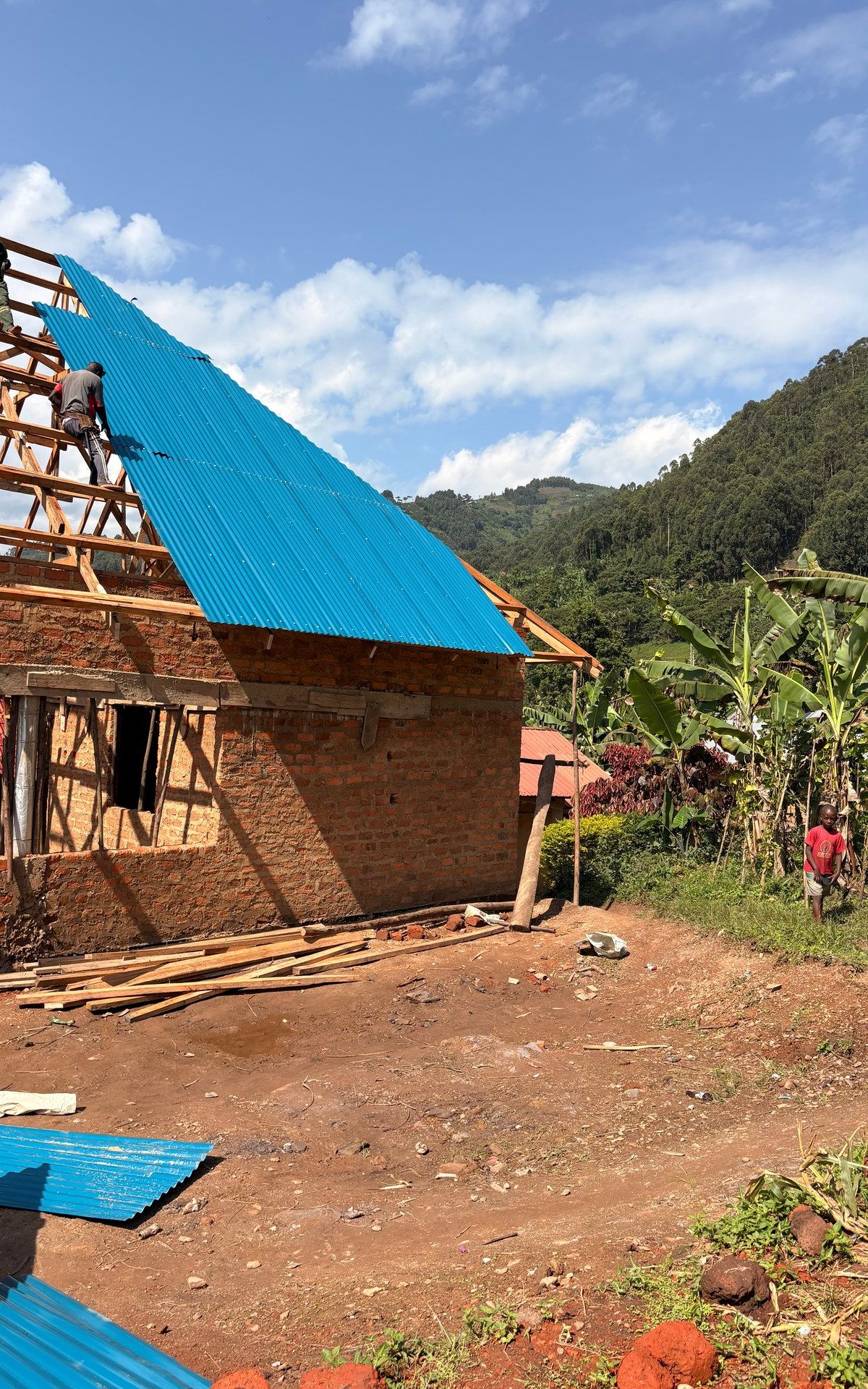 HopeKitchen Buhoma: Erste Grundmauern aus selbst gefertigten Ziegelsteinen, vor dem Hintergrund ugandischer Hügellandschaft. Foto: Mark Suer, Mai 2026, GPS: -0.9621°, 29.6106°