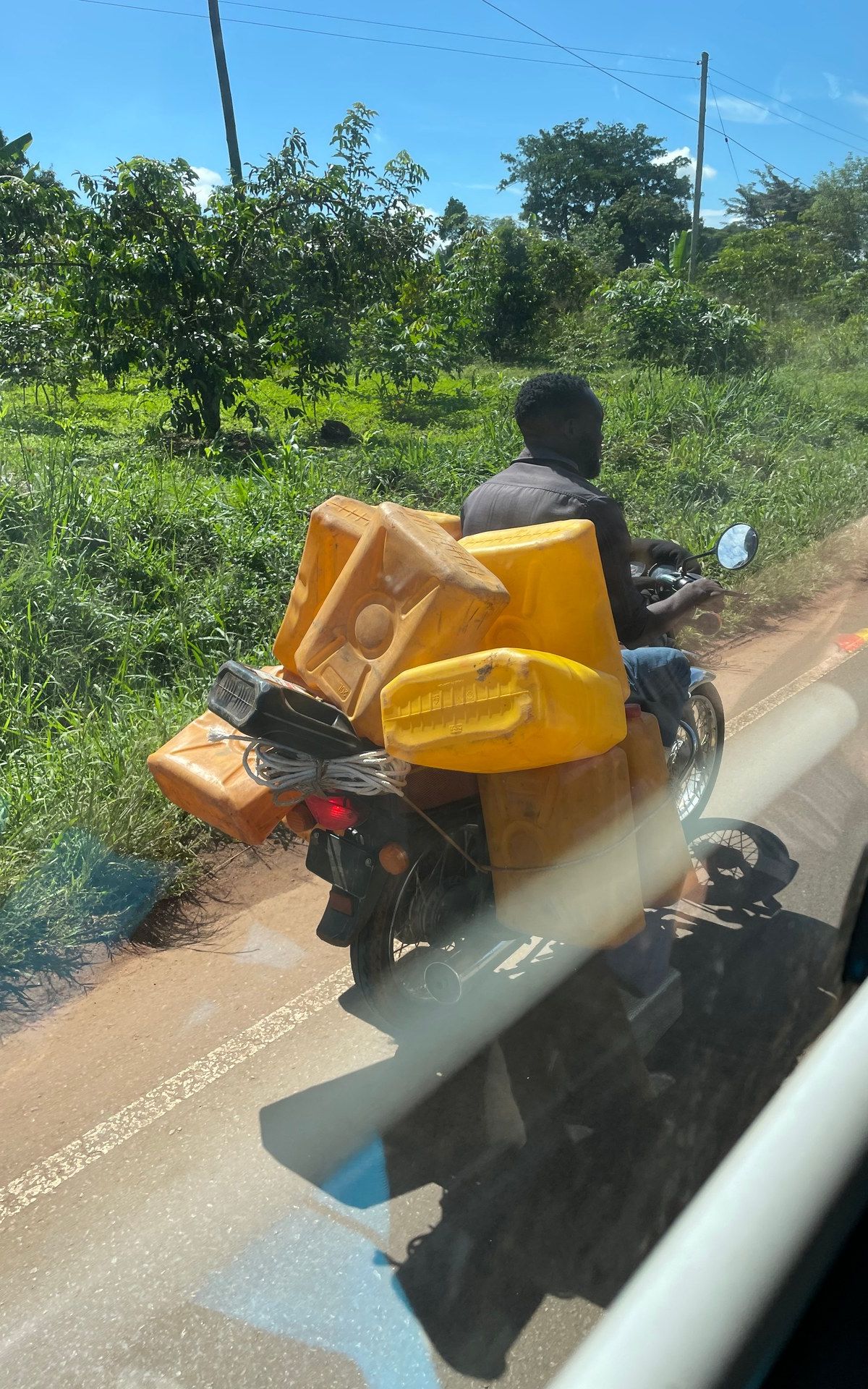 Boda-boda driver transporting water canisters on a rural road in Uganda — the everyday logistics of southwest Uganda, photographed October 2024