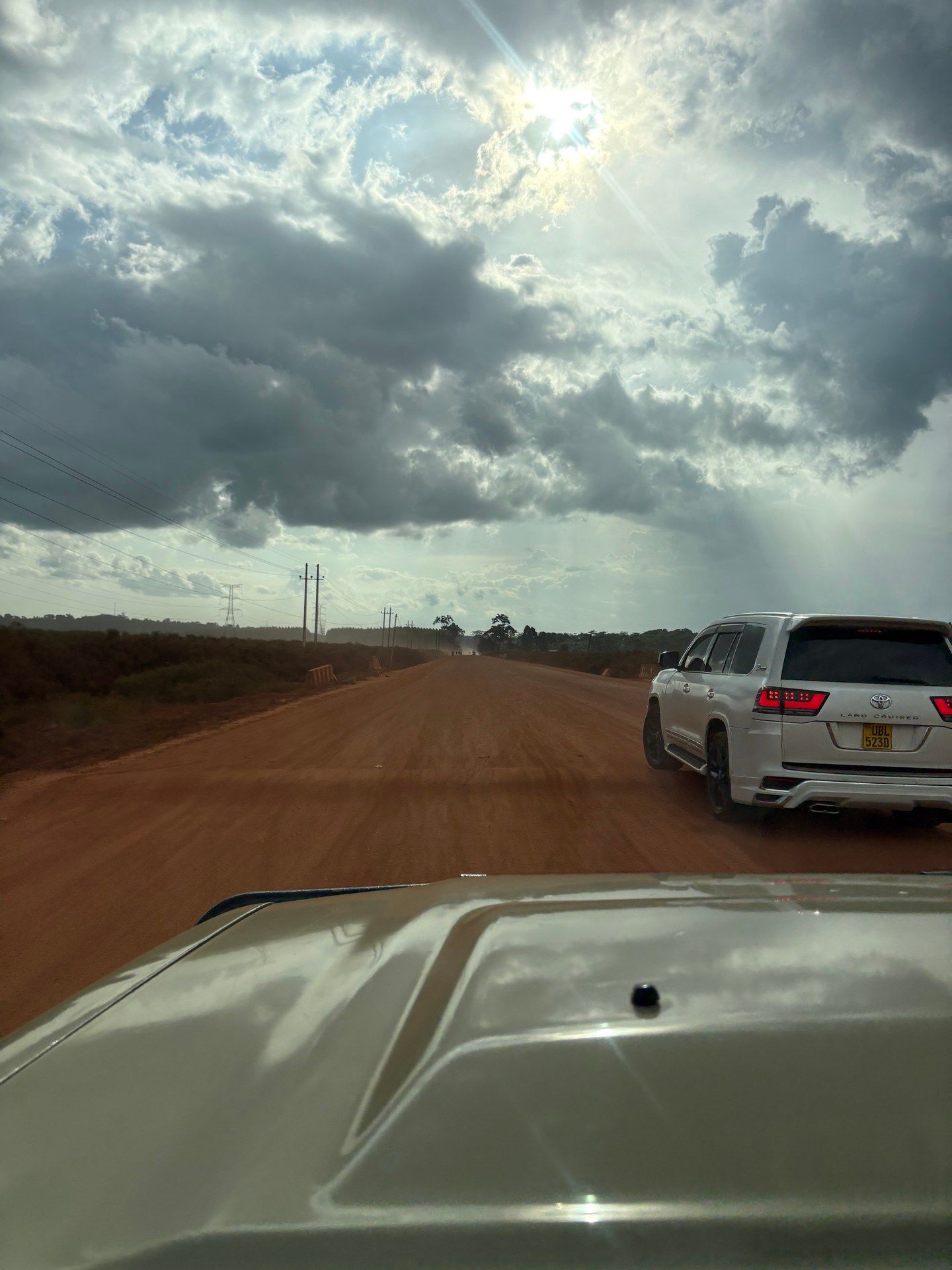 Red laterite road stretching toward the horizon through Ugandan countryside, a white safari jeep following ahead — the drive south toward Bwindi, January 2026